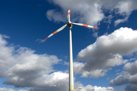 Ein Windrad im hessischen Vogelsberg dreht sich vor weiß-blauem Himmel.  
