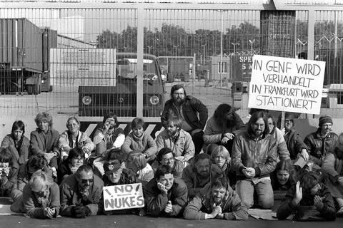 Mitglieder der Grünen, darunter auch Joschka Fischer (rechts neben dem Schild "No Nukes"), blockieren am 24.10.1983 ein US-Militärgelände im Frankfurter Stadtteil Hausen, das nach ihren Informationen für die Montage von Pershing II-Raketen vorgesehen sein sollte. Archivfoto: dpa