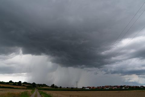 Dunkle Gewitterwolken und Regenschauer ziehen über eine Ortschaft hinweg.  Foto: Nicolas Armer/dpa