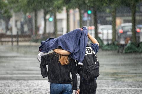 Zwei Passanten schützen sich mit einer Jacke vor einem der zahlreichen Regenschauer Foto: dpa