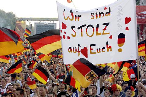 Deutsche Fans jubeln mit Nationalfahnen und halten ein Spruchband mit dem Schriftzug "Wir sind stolz auf Euch" beim Fanfest des FIFA World Cup 2006 während des Spieles um Platz drei zwischen Deutschland und Portugal. Foto: dpa 