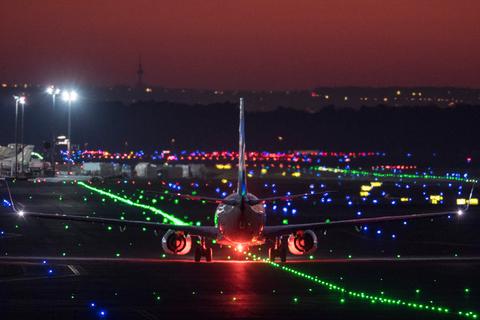 Ein Passagierflugzeug rollt im letzten Licht der untergehenden Sonne über die Rollbahn des Flughafens, während der Himmel rot leuchtet.  Symbolfoto: dpa/ Boris Roessler 
