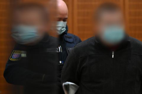 Der Angeklagte (rechts) wird zu Beginn eines Mordprozesses von einem Justizbeamten in den Gerichtssaal des Landgerichts Frankfurt geführt und spiegelt sich dabei in einer Plexiglasscheibe. Foto: dpa