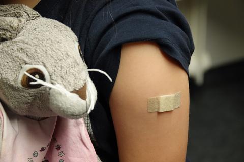 Ein Pflaster klebt nach der Corona-Impfung auf dem Arm eines Mädchens, das ein Kuscheltier in den Händen hält.  Symbolfoto: dpa