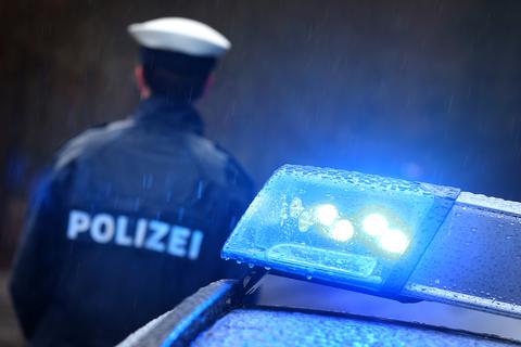 Ein Polizist steht im Regen vor einem Streifenwagen dessen Blaulicht aktiviert ist.  Symbolfoto: Karl-Josef Hildenbrand/dpa