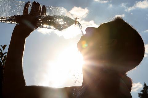 Eine Frau trinkt im Sonnenschein aus einer Wasserflasche. Foto: dpa